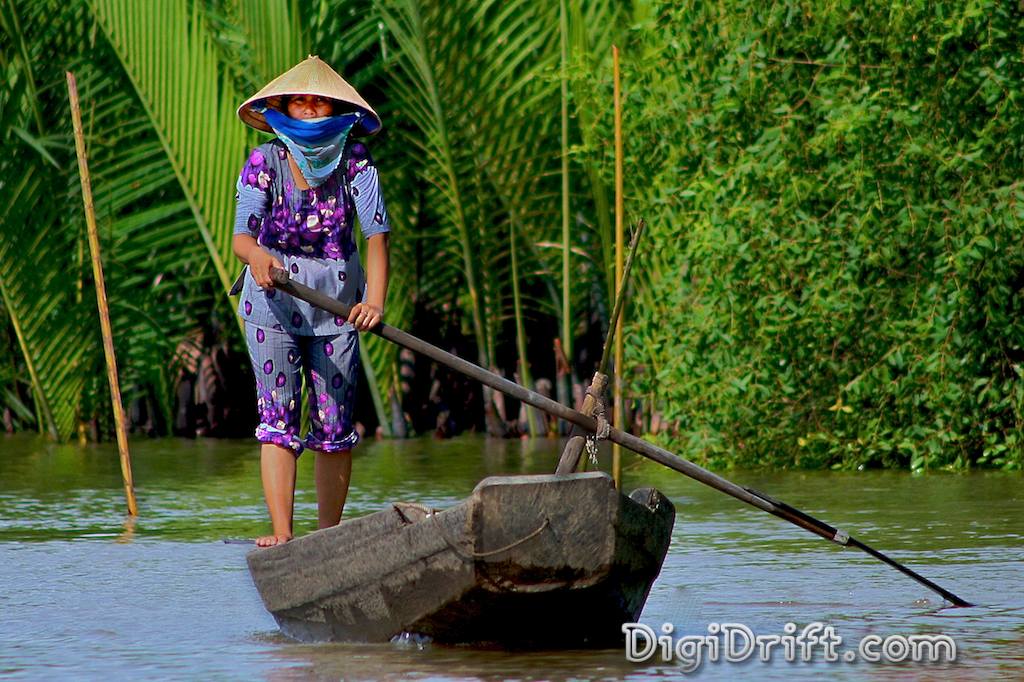 A woman in bright pruple clothes paddling a dugout in Vietnams Mekong Delta region